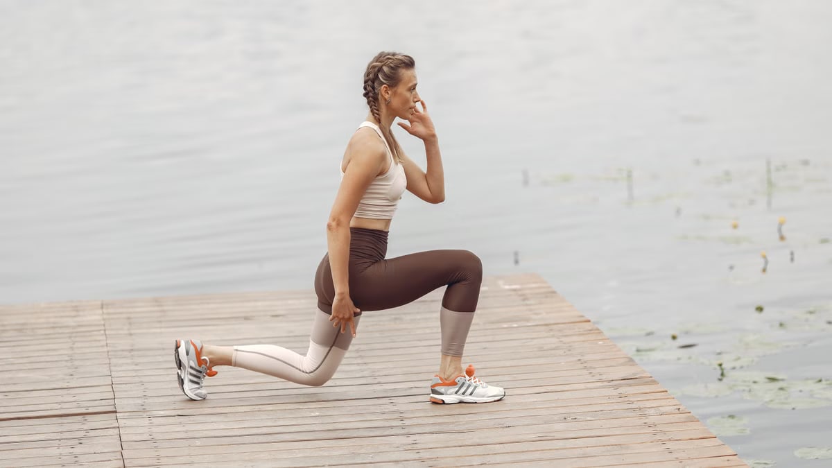 A woman performs lunges on a lakeside wooden deck, showcasing a fit lifestyle outdoors.